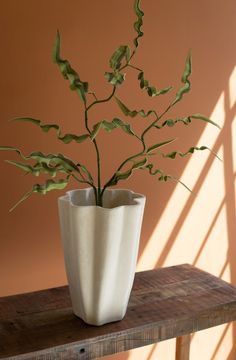 a plant in a white vase sitting on a wooden table next to a brown wall