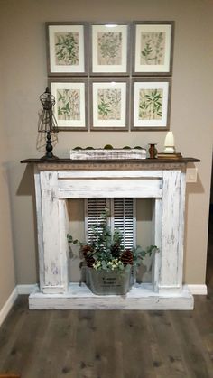 a white fireplace with pictures on the wall and potted plants in front of it