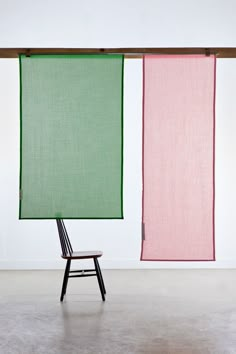 a chair sitting in front of two green and pink vertical blinds hanging from the ceiling