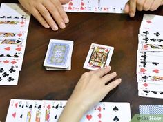 two people playing cards at a table with their hands on the deck and one person reaching for them