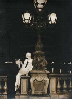 a woman sitting on top of a statue next to a lamp post in a dark room