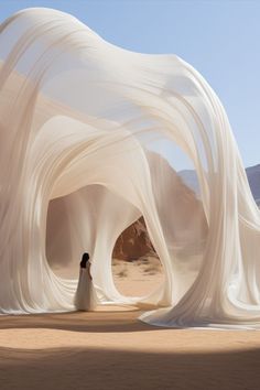 a woman is standing in front of an art installation with white fabric draped over it