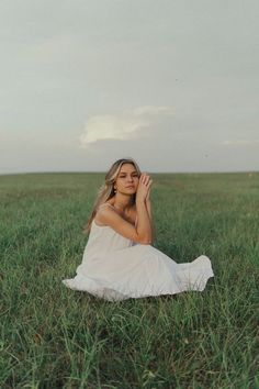 a woman sitting in the middle of a field with her hands up to her face