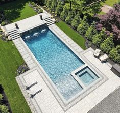 an aerial view of a swimming pool surrounded by lush green grass and trees with lounge chairs around it