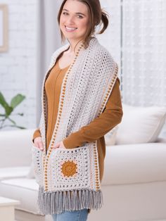 a woman standing in front of a white couch wearing a crocheted shawl