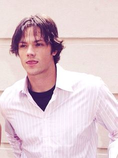 a young man in a white shirt and black tie standing next to a wall with his hands on his hips