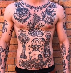 a man with many tattoos on his body and chest is standing in front of a brick wall