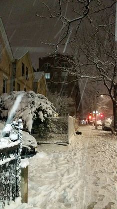 a snowy street with cars parked on the side and buildings in the background at night