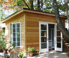 a small wooden house with white doors and windows on the outside, surrounded by trees