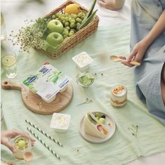 a woman sitting at a table with food and drinks on it, in front of a basket full of fruit