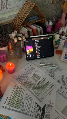 a laptop computer sitting on top of a table covered in papers and candles next to books