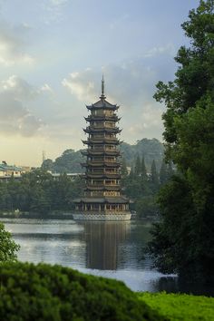 a tall tower sitting on top of a lake next to lush green trees and bushes