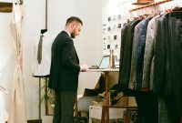 a man standing in front of a closet full of suit and tie racks, looking down at his pants