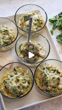 four glass bowls filled with food sitting on top of a white tray next to spinach leaves