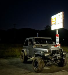 a jeep is parked in front of a gas station sign at night with the lights on