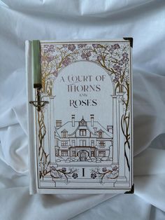 a court of horns and roses book sitting on top of a white sheet covered bed