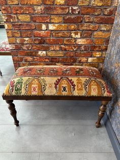 an old bench sitting in front of a brick wall with a colorful rug on it