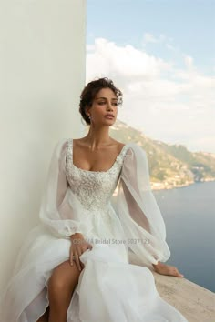 a woman sitting on top of a wall wearing a white dress