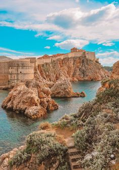 an old castle sitting on top of a cliff next to the ocean with stairs leading up to it