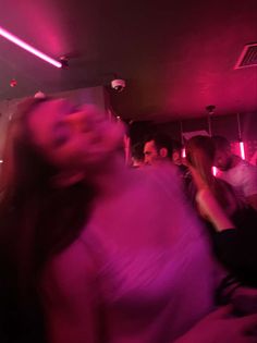 a woman in a pink dress is dancing at a party with other people and lights behind her