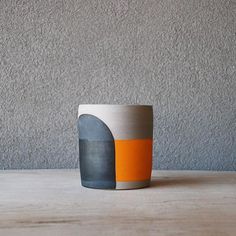 an orange and grey cup sitting on top of a wooden table next to a gray wall