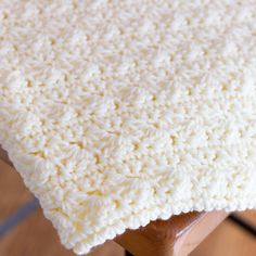 a white crocheted blanket sitting on top of a wooden chair next to a table