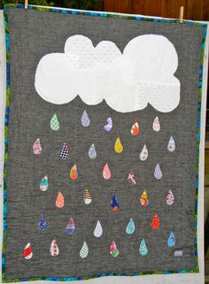 a quilt hanging on a clothes line with clouds and raindrops