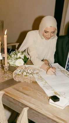 a man and woman sitting at a table writing on paper with candles in the background