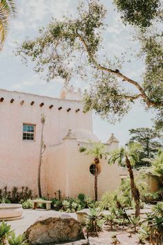 a pink building with palm trees in the foreground and a stone bench on the ground