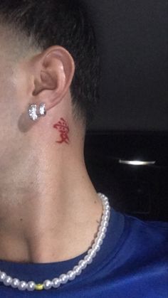 a man with a red tattoo on his neck and behind his ear is a pearl necklace