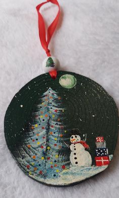 a christmas ornament with a snowman and tree painted on it's side