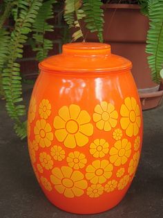 an orange vase with yellow flowers painted on it next to a potted fern plant