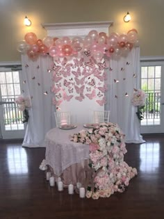 a table topped with lots of pink balloons and flowers next to a white wall covered in butterflies