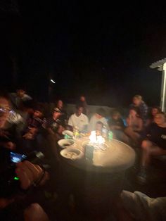 a group of people sitting around a table with a lit candle on top of it