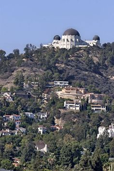 a large white building on top of a hill surrounded by trees and buildings in the background