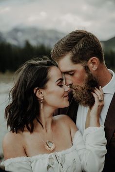 a man and woman standing next to each other in front of a mountain lake kissing