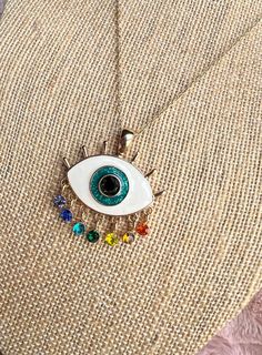 Broaden your horizons in style with new jewelry from Cosmic Created Magic! Look like pure magic while feeling protected wearing the rainbow evil eye necklace. Hanging from a gold chain is a stunning evil eye gold pendant. Gold eyelashes surround the white of the eye. The iris is a sparkly light blue with a round black rhinestone for the pupil. Hanging below the eye are a purple, dark blue, light blue, green, yellow, orange, and red gems representing each chakra. Show off your vibrant side with confidence. This necklace is a gift that will look and feel good! Black Rhinestone, Evil Eye Necklace, Eye Necklace, Evil Eye, Gold Pendant, Gold Chains, Eyelashes, Violet, Necklace Etsy