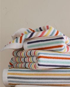 a stack of multicolored towels sitting on top of a wooden table next to a white wall