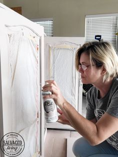 a woman is painting the inside of a refrigerator with white paint on it and she is holding a spray bottle in her right hand