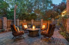 an outdoor patio with chairs, fire pit and brick pavers flooring is lit up at night