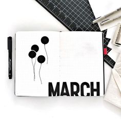 an open notebook with the word march written in black on it next to markers and pencils