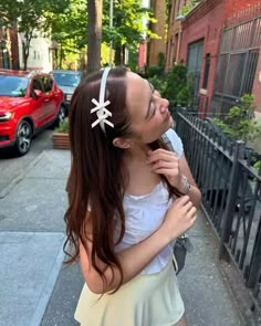 a woman is standing on the sidewalk with her hair tied back and wearing a white headband