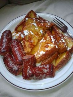 a white plate topped with french toast covered in syrup and powdered sugar next to a fork