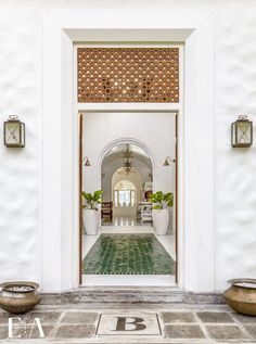 an entrance to a white building with potted plants on either side and doors open