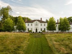 a large white house sitting in the middle of a lush green field next to trees