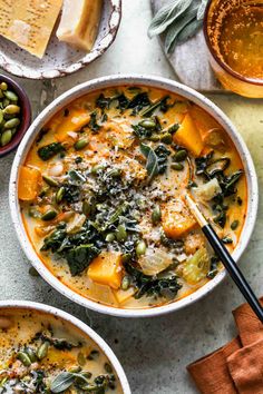 two bowls of vegetable soup with cheese and bread on the side, next to other dishes