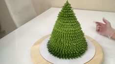 a fake green christmas tree sitting on top of a white table next to a person's hand