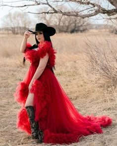 a woman in a long red dress and cowboy hat poses for a photo with her hand on her head