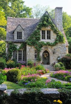 a stone house with flowers and bushes around it