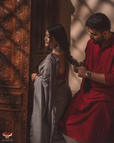 a man and woman standing next to each other in front of a wooden door looking at something